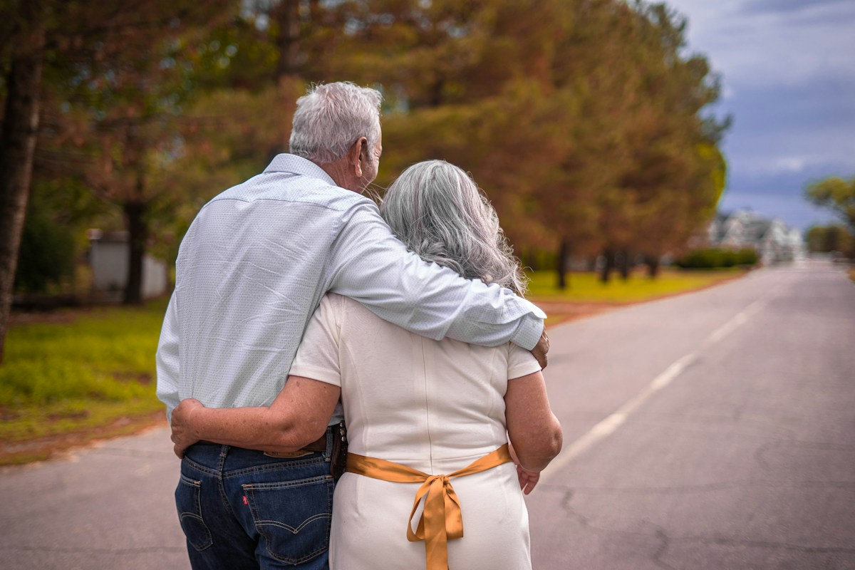An older couple walking together with their arms around each other
